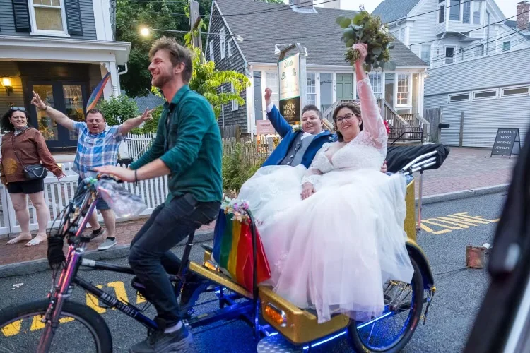 A wedding couple celebrating in a pedicab as onlookers cheer.