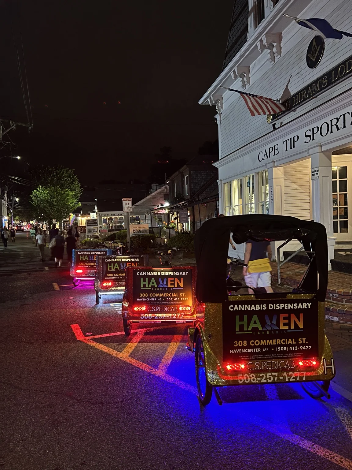 Illuminated pedicab advertising on Commercial Street after dark.