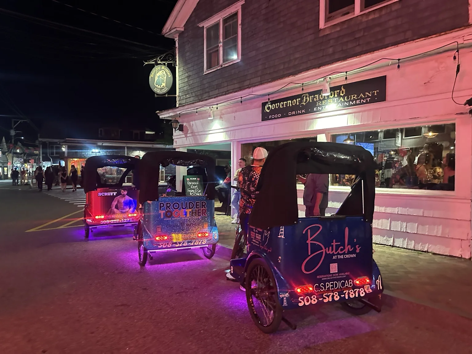 Covered, illuminated pedicabs outside a restaurant at night.