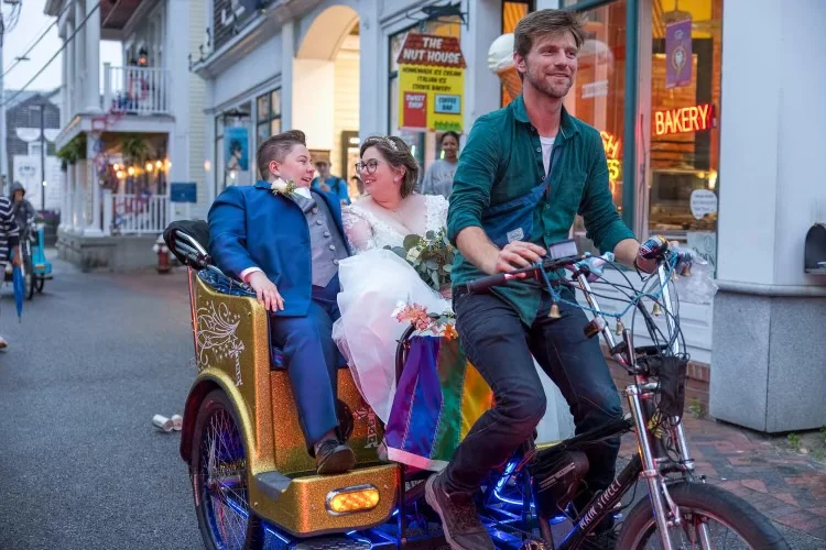 A smiling wedding couple and their pedicab rider on Commercial Street.